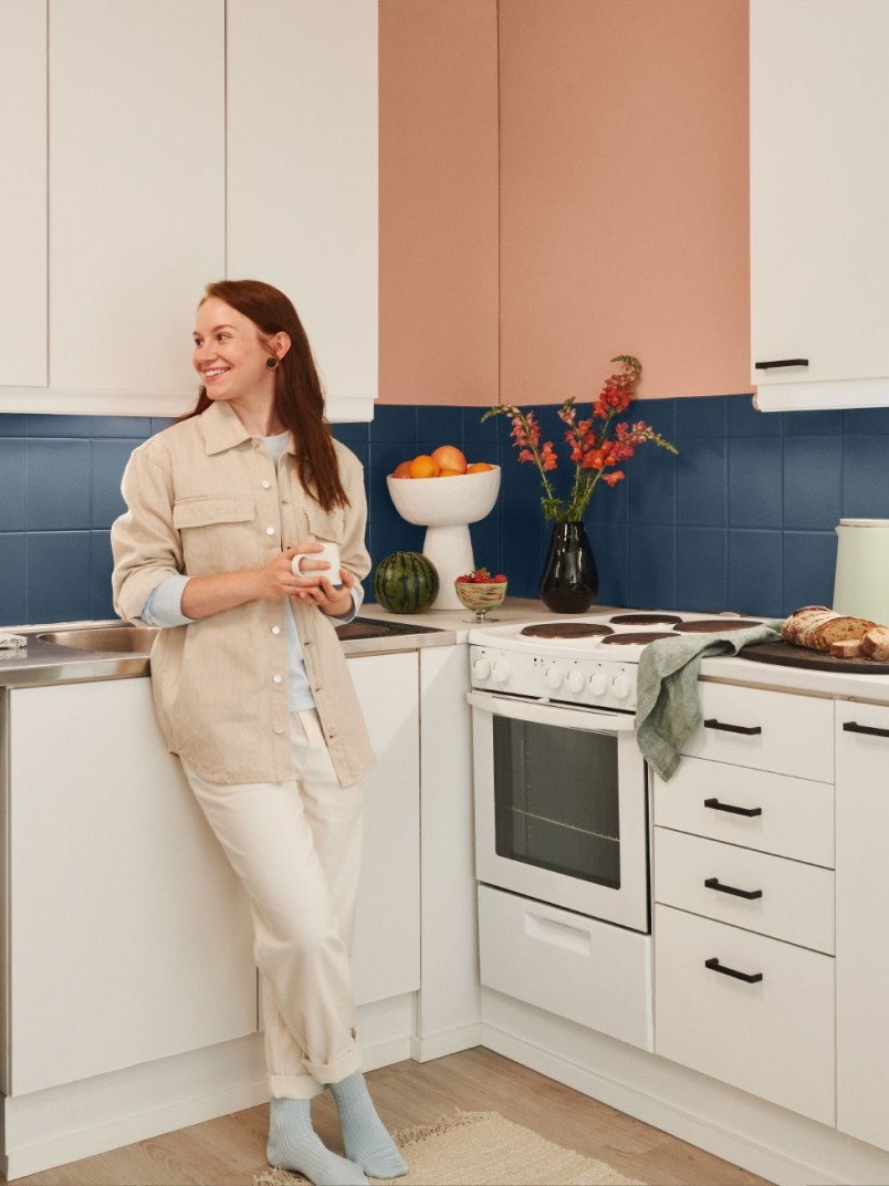 woman in white kitchen with blue backsplash and peach colour wall