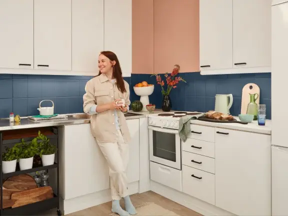 woman in white kitchen with blue backsplash and beige wall
