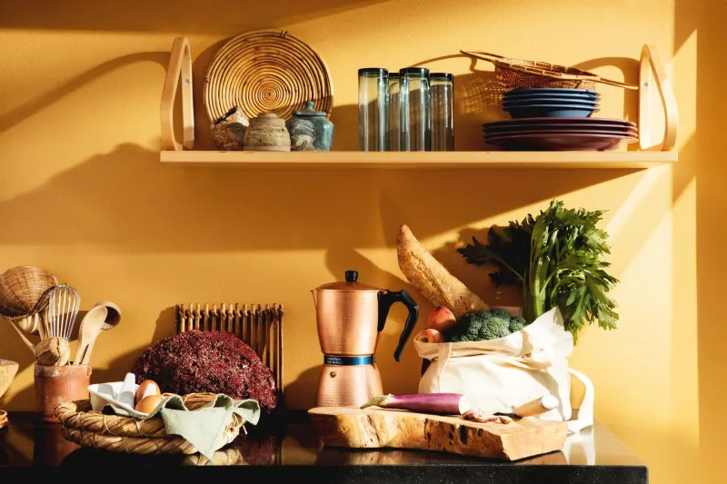 bright warm yellow wall behind busy kitchen desk and shelf